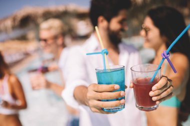 Bir grup mutlu arkadaş havuzda kokteyllerle dans ediyor.