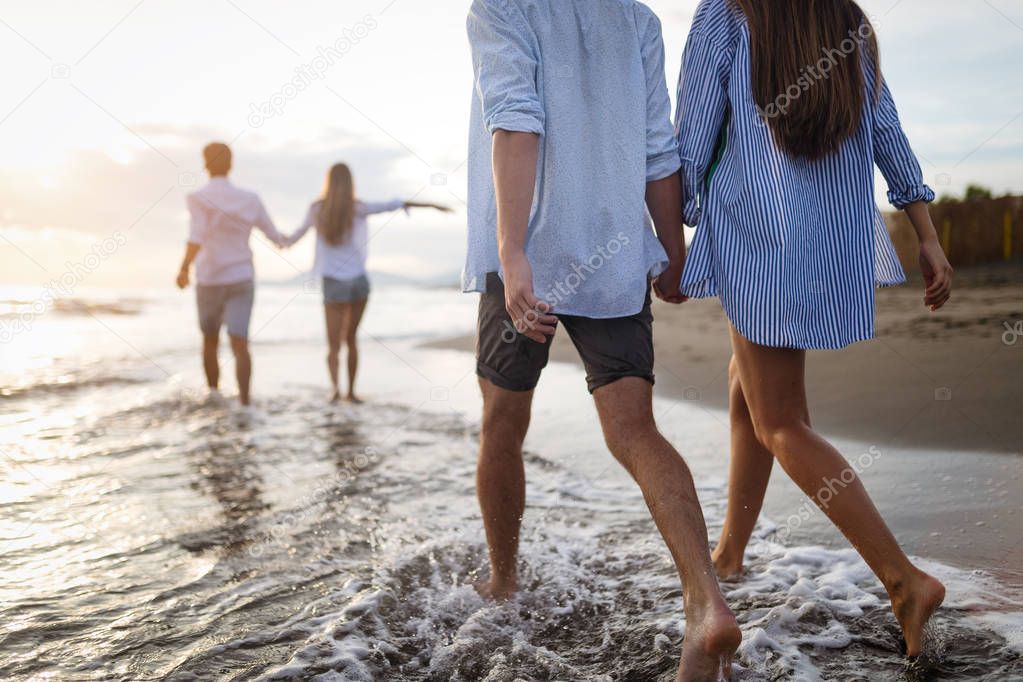 Group of friends having fun on the beach under sunset sunlight.