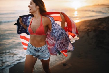 Sahilde neşeli, heyecanlı bir kadın elinde Amerikan bayrağı, eğleniyor..