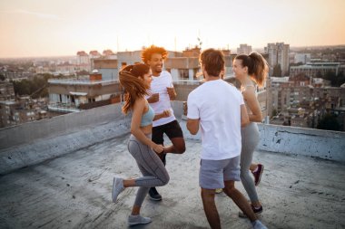 Sportif ve güler yüzlü. Bir grup atletik genç, spor giyimli arkadaşlar egzersiz yapıyor. Spor açık havada