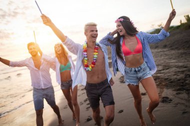 Bir grup arkadaş gün batımında plajda havai fişek yakıp özgürlüğün tadını çıkarıyorlar.