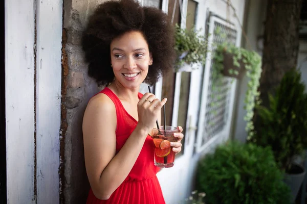 Lifestyle fashion portrait of black woman posing on the street with drink