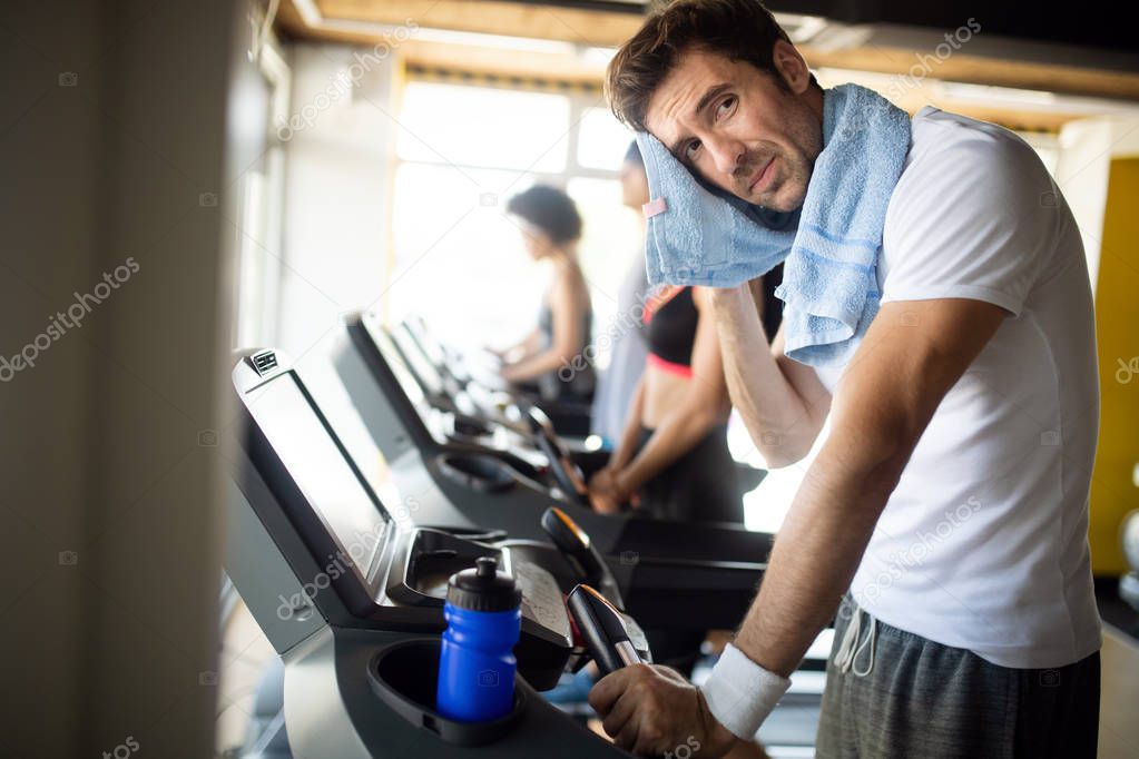 Athletic young man having rest after running training, drinking water at gym at treadmill