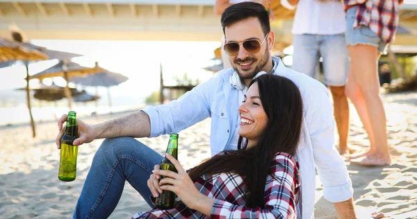 幸せな若いカップルはビールを飲んで 日没の間にビーチで楽しんでいます — ストック写真