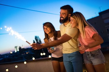 Bir grup arkadaş, kıvılcımlarla çatı partisinin tadını çıkarıyor. Eğlenen gençler