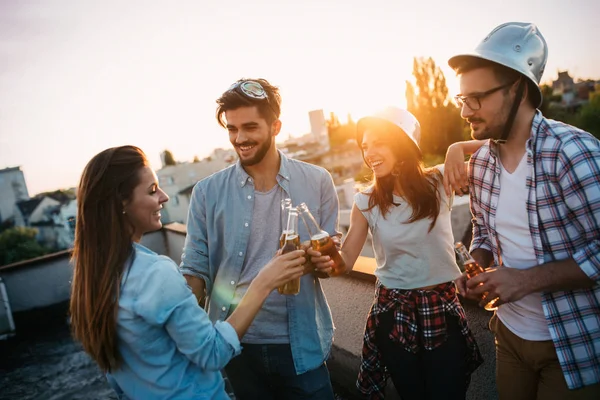 Young people partying on terrace with drinks at sunset. Young men and women enjoying drinks on rooftop