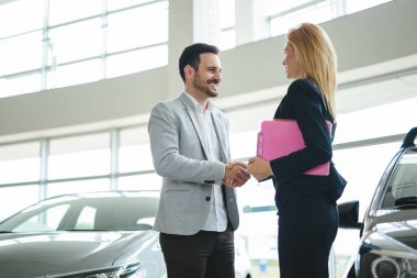 Satıcı salonda potansiyel müşteriye yeni bir araba modeli gösteriyor.