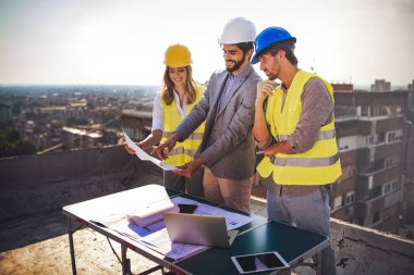 Mimarlar ve mühendislerden oluşan bir ekip inşaat sahasındaki kontrol belgelerini inceleyen gruptakiler.