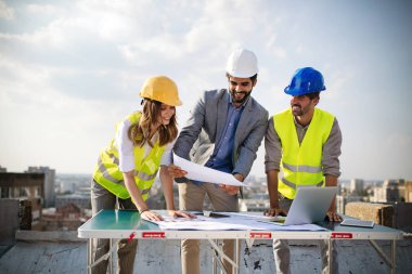 Mimarlar ve mühendislerden oluşan bir ekip inşaat sahasındaki kontrol belgelerini inceleyen gruptakiler.
