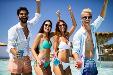 Bir grup mutlu arkadaş havuzda kokteyllerle dans ediyor.