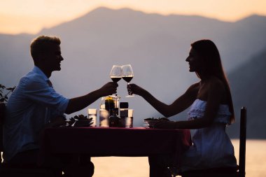 Genç çift, tropik bir tatil köyünde romantik bir gün batımı yemeği yiyor.