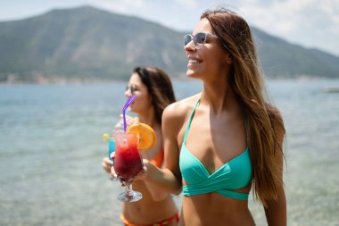 Güzel genç kızlar kokteyller yaz tatili kumsalda içme.