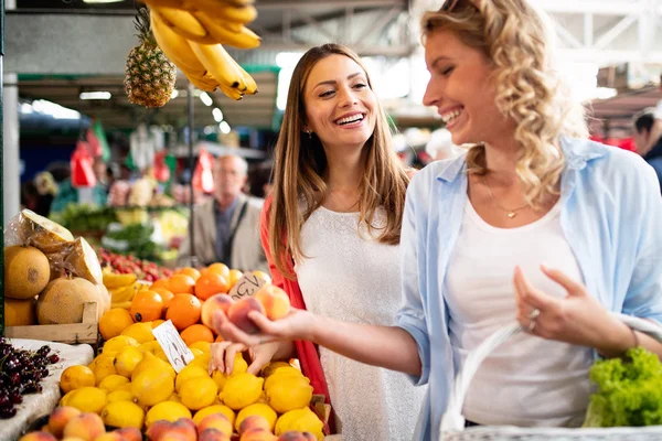 Young happy healthy women shopping vegetables and fruits on the market