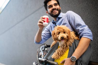 Bisiklet üzerinde oturan ve köpek ile sokakta kahve bardağı tutan yakışıklı genç adam