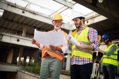 İnşaat alanı kontrol belgeleri ve iş akışı üzerine grup halinde çalışan mimarlar ve mühendisler.