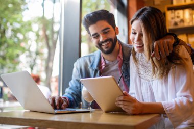 Üniversitede kafede dizüstü bilgisayar kullanarak gülümseyen arkadaşlar