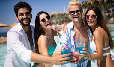 Bir grup mutlu arkadaş havuzda kokteyllerle dans ediyor.