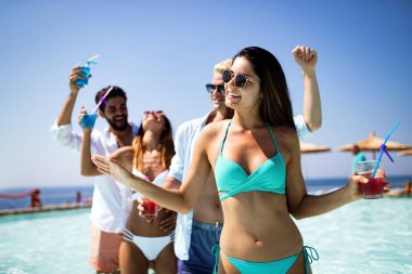 Bir grup mutlu arkadaş havuzda kokteyllerle dans ediyor.