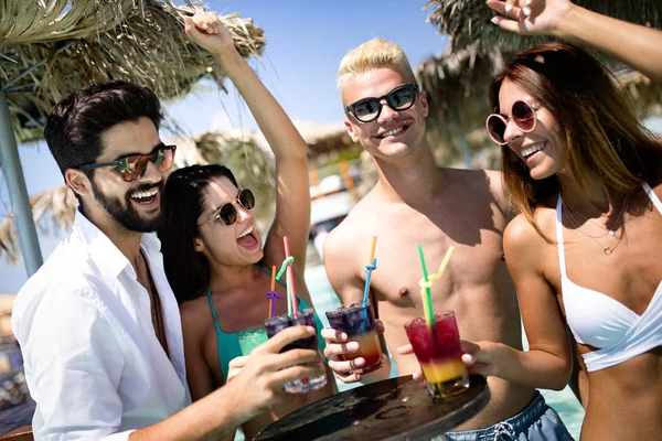 Group of happy friends having fun dancing at swimming pool with cocktails