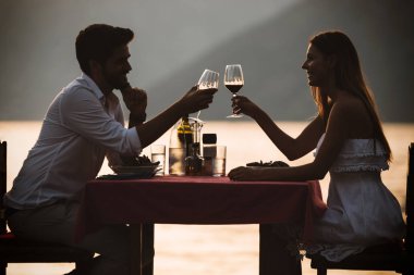 İnsanlar, kutlama, tatil, balayı ve romantizm konsepti. Genç çift sahilde romantik bir akşam yemeği yiyor..