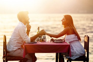 İnsanlar, kutlama, tatil, balayı ve romantizm konsepti. Genç çift sahilde romantik bir akşam yemeği yiyor..