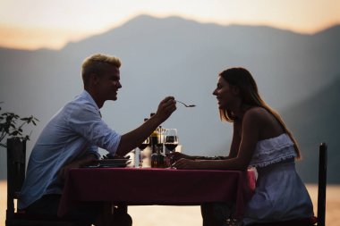 İnsanlar, kutlama, tatil, balayı ve romantizm konsepti. Genç çift sahilde romantik bir akşam yemeği yiyor..