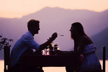 Genç çift sahilde romantik gün batımı akşam yemeği paylaşımı