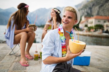 Mutlu arkadaşlar grubu plaj partisinde gün batımında kokteyl içerek eğleniyor. Tatildeki gençlerle yaz neşesi ve arkadaşlık konsepti