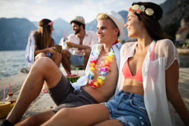 Mutlu arkadaşlar grubu plaj partisinde gün batımında kokteyl içerek eğleniyor. Tatildeki gençlerle yaz neşesi ve arkadaşlık konsepti