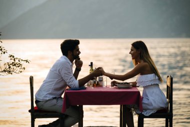 Genç çift sahilde romantik gün batımı akşam yemeği paylaşımı