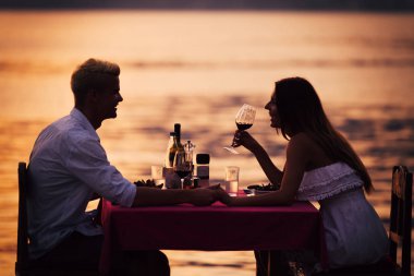 Genç çift, tropik bir tatil köyünde romantik bir gün batımı yemeği yiyor.