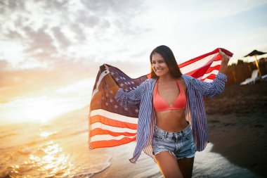 Sahilde neşeli, heyecanlı bir kadın elinde Amerikan bayrağı, eğleniyor..