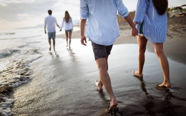 Mutlu arkadaş grubu plajda gün batımında tatilin tadını çıkarıyor.