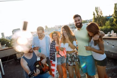 Bir çatı partisinde eğlenen, gitar çalan, şarkı söyleyen, dans eden ve sakinolan genç arkadaşlar