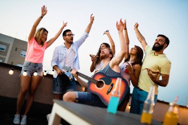 Bir çatı partisinde eğlenen, gitar çalan, şarkı söyleyen, dans eden ve sakinolan genç arkadaşlar