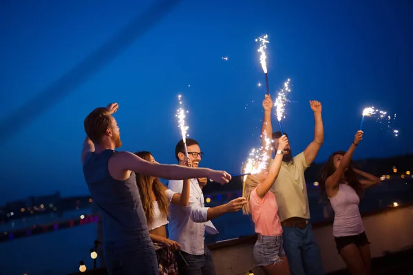 Group of friends enjoying a rooftop party and dancing with sparklers