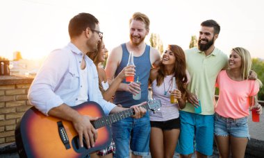 Bir çatı partisinde eğlenen, gitar çalan, şarkı söyleyen, dans eden ve sakinolan genç arkadaşlar