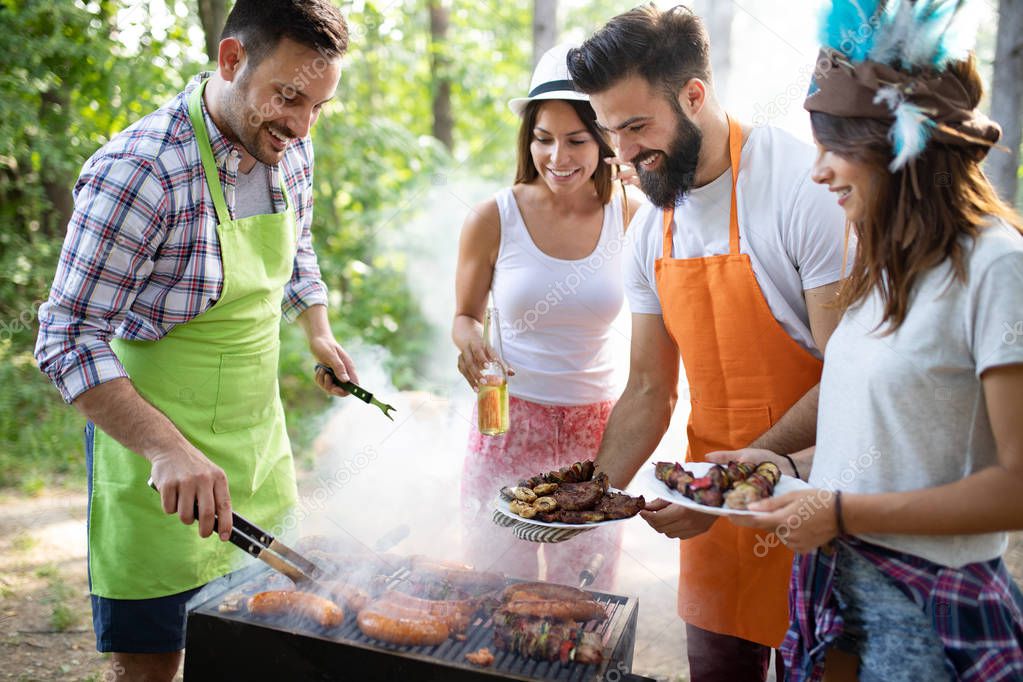 Group of happy friends eating and drinking beers at barbecue dinner outdoors