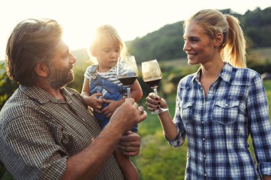Üzüm bağında kırmızı şarap içip eğlenen insanların fotoğrafı.