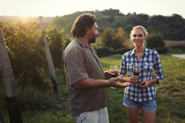 Üzüm bağında kırmızı şarap içip eğlenen insanların fotoğrafı.