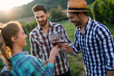 Üzüm bağında kırmızı şarap içip eğlenen insanların fotoğrafı.