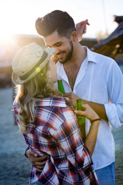 Kumsalda gülümseyen ve bira içen mutlu genç çift