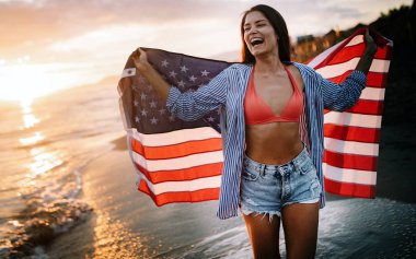 Sahilde neşeli, heyecanlı bir kadın elinde Amerikan bayrağı, eğleniyor..