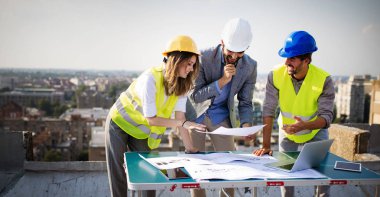 Mimarlar ve mühendislerden oluşan bir ekip inşaat sahasındaki kontrol belgelerini inceleyen gruptakiler.