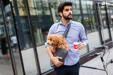 Bisiklet üzerinde oturan ve köpek ile sokakta kahve bardağı tutan yakışıklı genç adam