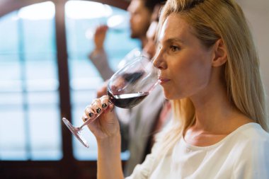 Beautiful blonde woman drinking glass of red wine indoors clipart