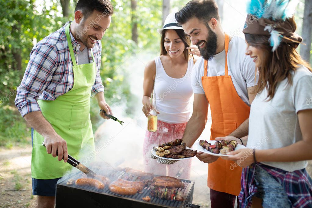 Group of happy friends eating and drinking beers at barbecue dinner outdoors