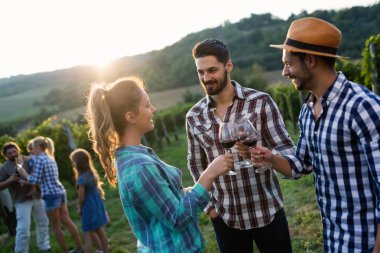 Üzüm bağında kırmızı şarap içip eğlenen insanların fotoğrafı.