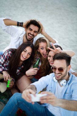 Arkadaş grubu plaj partisi. Neşeli genç insanlar güzel birlikte sahilde vakit ve bira içmek