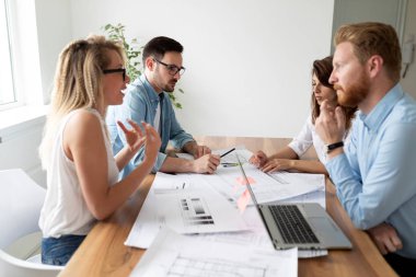 Ofis masasında birlikte otururken çalışan ve iletişim kuran bir grup iş adamı.